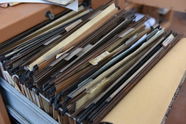 Overflowing filing cabinet drawer packed with stacked paper documents and folders