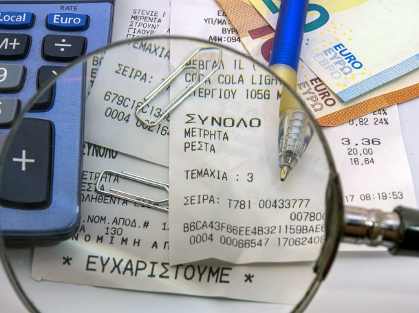 Magnifying glass over printed receipts beside a calculator, pen, and euro banknotes