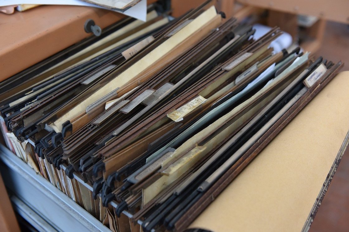 Open filing cabinet drawer packed with labeled folders representing physical document storage