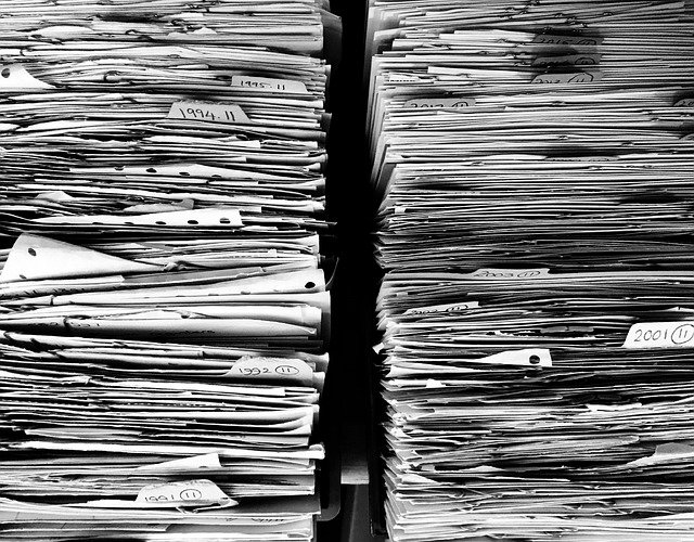 Black and white photo of tall stacks of paper documents labeled by year in filing trays