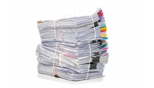 Large stacked pile of paper documents bound with rubber bands and binder clips