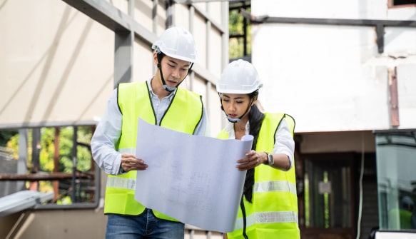 Two construction workers in hard hats reviewing blueprints at a building site