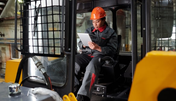 Construction worker in orange hard hat using a tablet inside heavy machinery cab