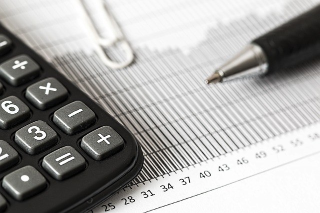 Calculator, pen, and paper clip resting on a financial document with ruler