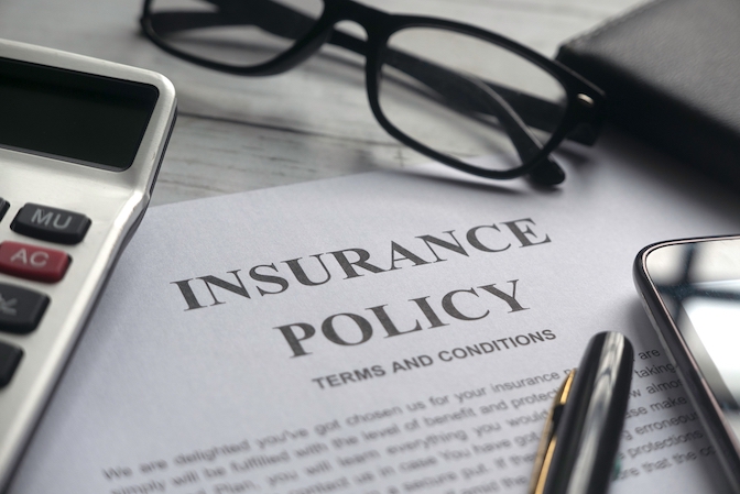 Printed insurance policy document with terms and conditions on a desk beside glasses, pen, and calculator