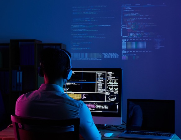 Software developer working at night with multiple monitors displaying colorful code