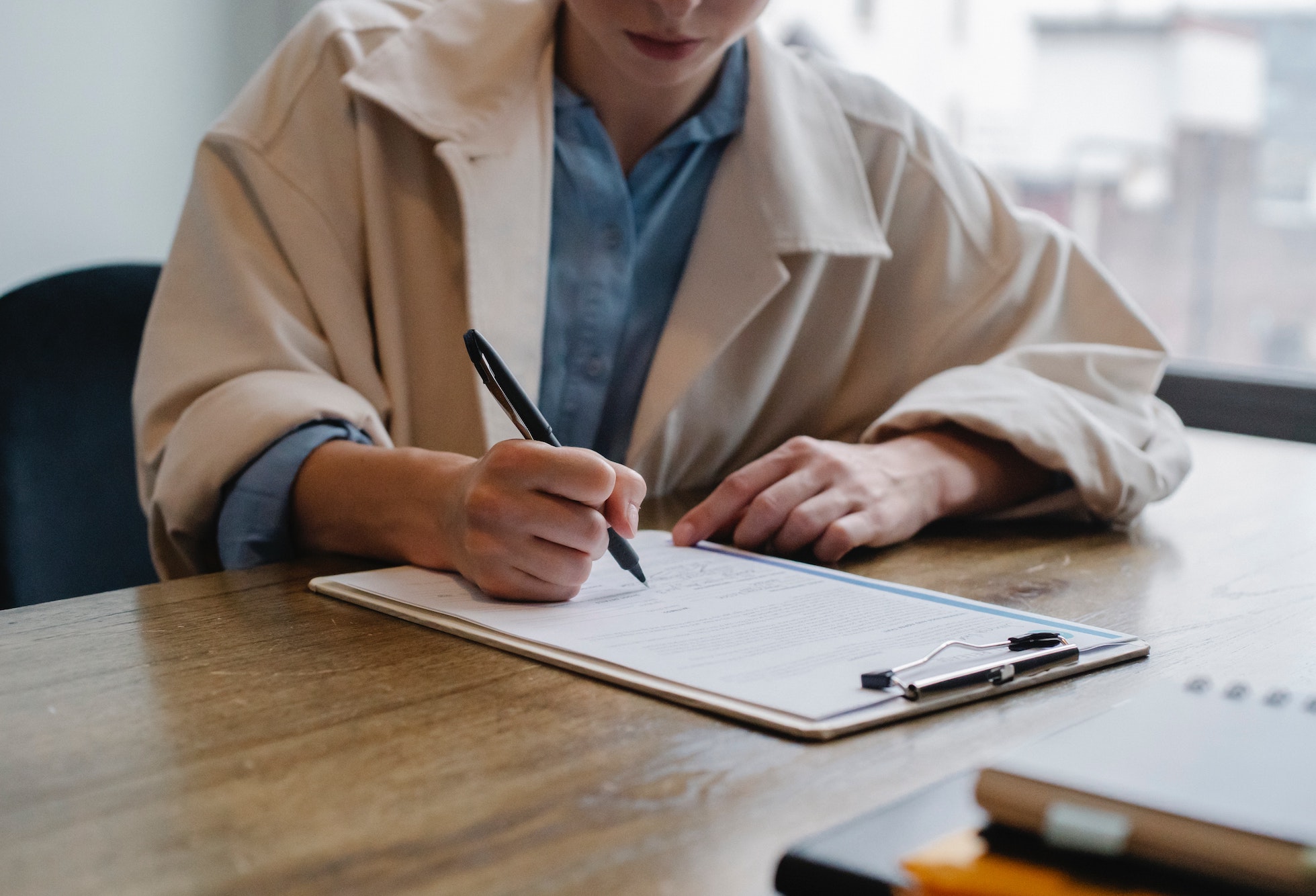 HR professional in beige blazer writing on a resume document at a wooden desk